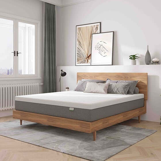 A white and grey mattress on a wooden bed frame in a brightly lit, modern bedroom with minimalist decor and art on the wall